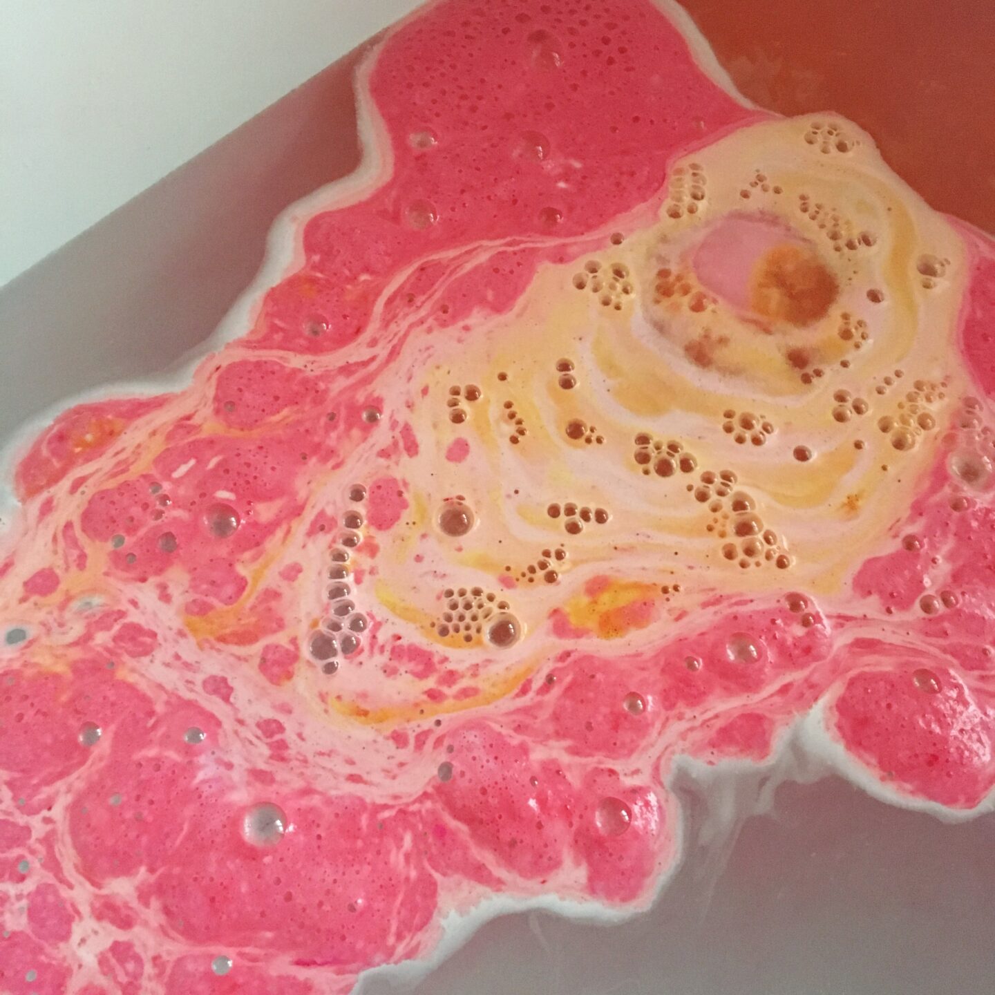 lush Christmas sweater bath bomb in water showing bright pinks and orange.