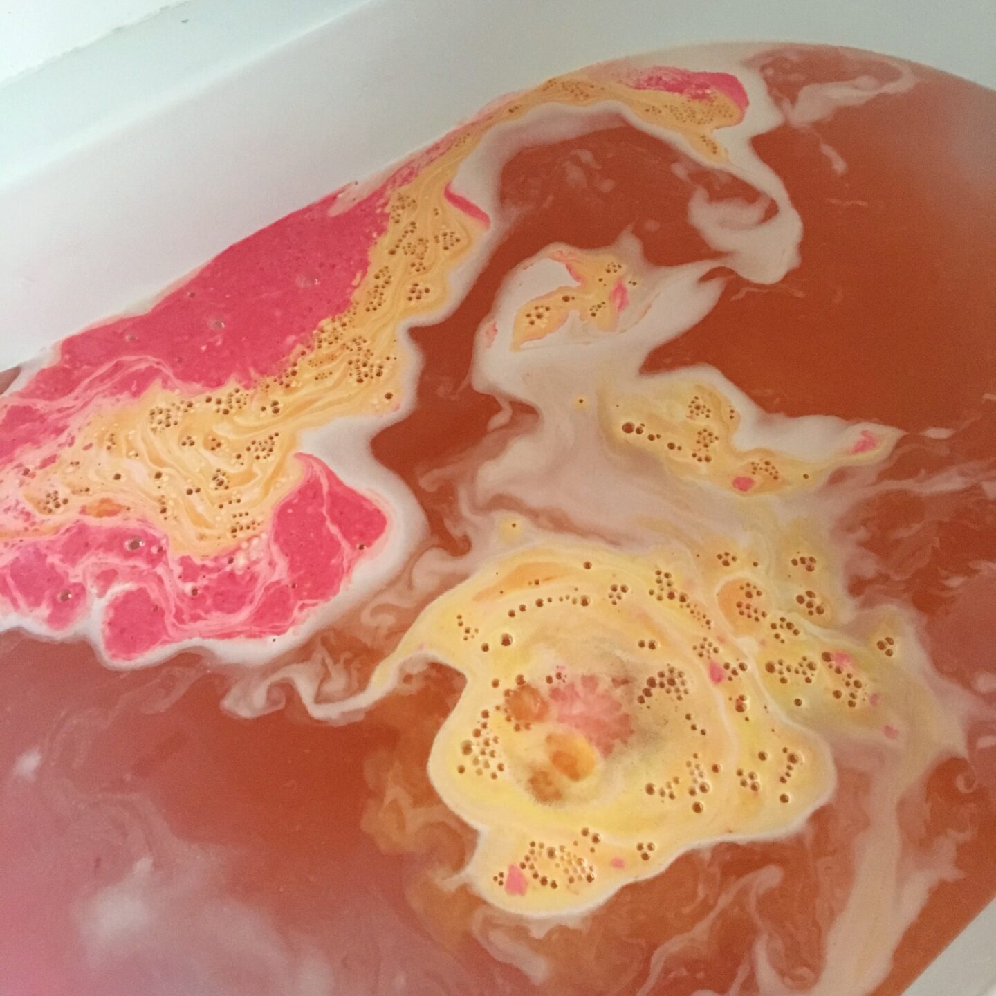 bath bomb in water, showing some of the original colours, but the orange/ pink of the final bath colour