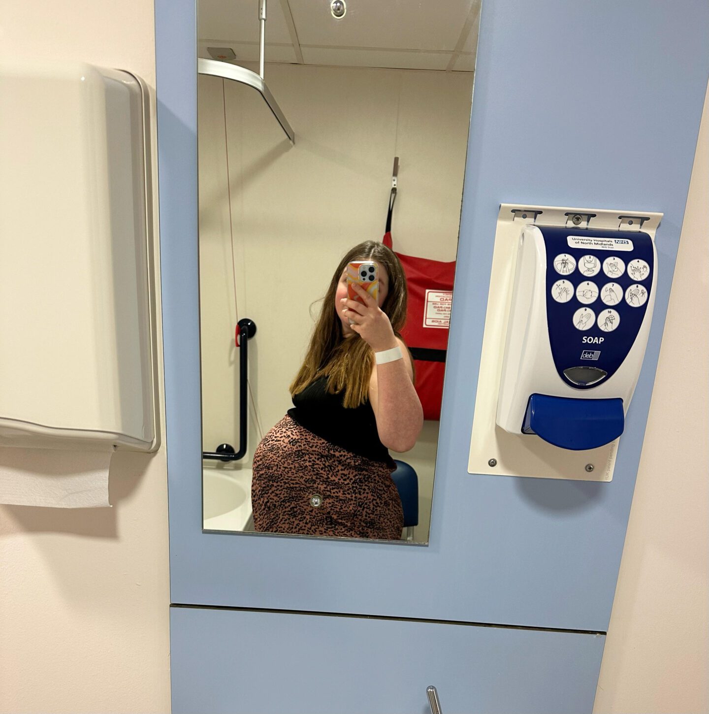 My birth story | Selfie with phone covering face, showing baby bump. Wearing a black top and a brown skirt with black spots.