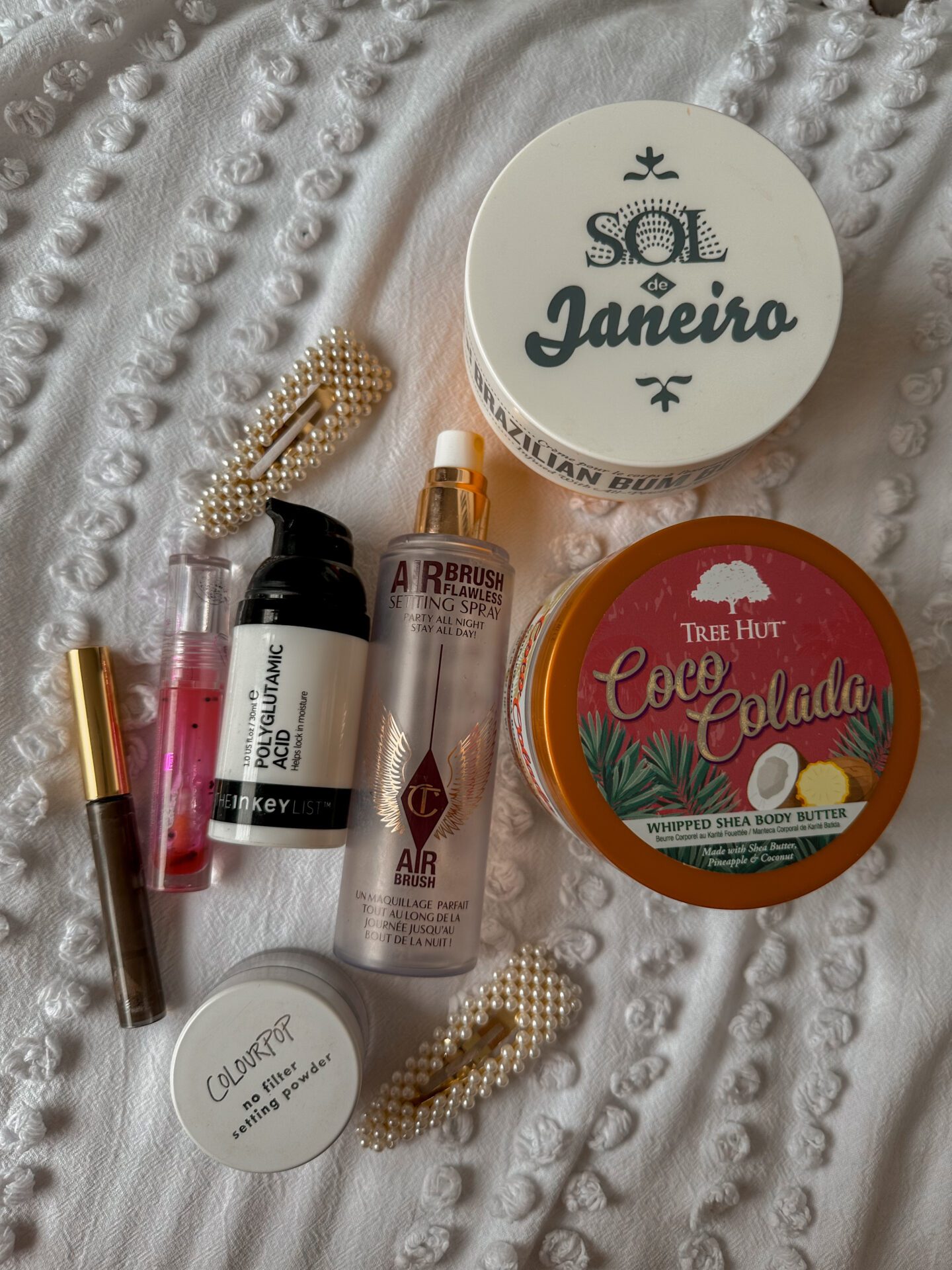 Makeup and skincare products laid out on a white background. Brands include sol de janeiro, the inkey list, Tree hut