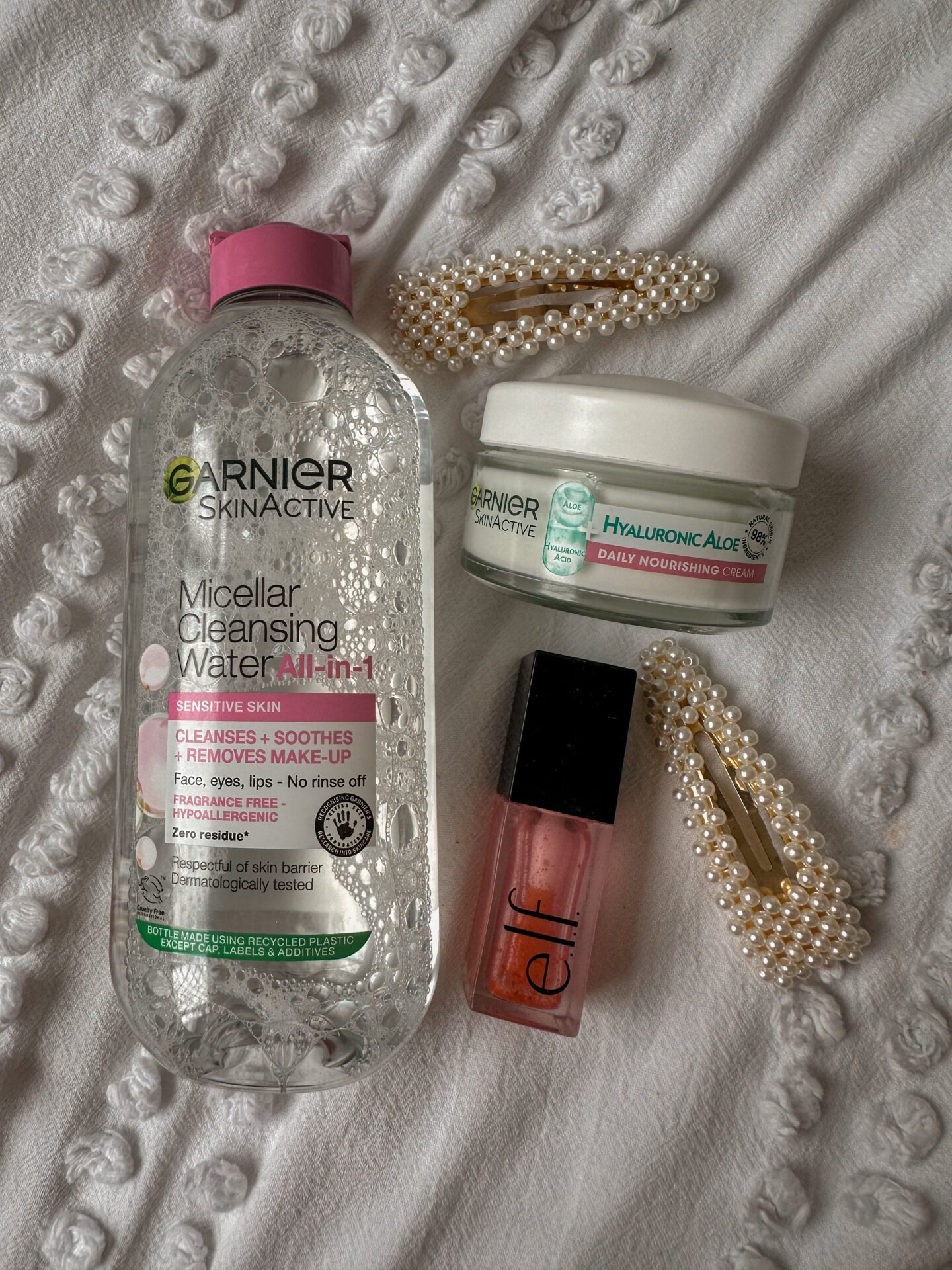 skincare products on a white background with two pearl clips. Garnier Micellar water, Garnier moisturiser, elf lip oil.